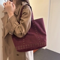 Burgunderfarbene Wildleder-Tote Bag mit Metallösen, getragen von einem Modell im Trenchcoat - Rot