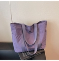 Detail der lila Nylon-Tragetasche auf Ledersofa mit seitlichem Markenlabel und Metallschnalle - Lila