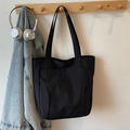 Minimalist black canvas tote bag with embroidery, hanging in a cozy home setting - Black