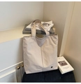 Close-up of beige waterproof canvas tote bag with a circular metal logo and pleated texture - Off White