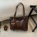 Detail van een bruine leren shopper met glanzende vintage textuur en een kralenhanger - Bruin