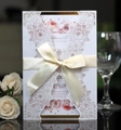 Dettaglio dell'invito di nozze tagliato al laser con nastro di seta beige e fiori - Bianco