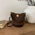 Vintage bruine bucket bag van suède en leer met gouden plaatje op houten ondergrond - Bruin