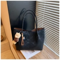 Detail of a black suede tote bag with a bear charm on a wooden step with soft lighting - With Charm / Black