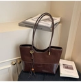 Detalle de bolso tote marrón oscuro mostrando mezcla de gamuza, cuero y accesorio borla - café