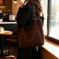 Sac cabas en daim marron foncé avec rivets argentés présenté dans un décor de café relaxant - Marron