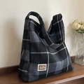Black and grey plaid flannel tote bag with a bear leather patch on a wooden desk - Black