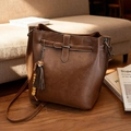 Vintage brown leather bucket bag with tassel charm on a dark wooden floor - Brown