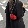 Red shell-shaped crossbody bag with glossy finish and gold chain strap on model - Red