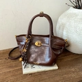 Bolso tipo cubo vintage en cuero marrón con cierre dorado y borla sobre libros - Marrón