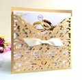 Nahaufnahme der lasergeschnittenen goldenen Hochzeitseinladung mit weißer Satinschleife - Beige Gold
