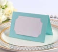 Détail d'un marque-place de mariage bleu ajouré posé sur une assiette à bordure dorée - Bleu Pâle Perlé