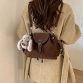 Mini mochila de ante marrón con colgante de conejo sobre un abrigo beige con textura - Café con Colgante