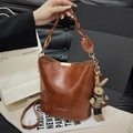 Borsa a secchiello marrone vintage con manico intrecciato e ciondolo a coniglio, in mano - Marrone con ciondolo
