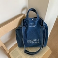 Grande borsa tote in denim blu scuro con tracolla regolabile appoggiata su sedia - Blu scuro