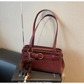 Detail der burgunderroten Schultertasche mit Zierschnalle und weichem Plüschkugel-Anhänger - Weinrot Mit Anhänger