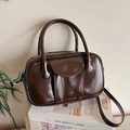 Brown patent leather bowling bag with top handles and a crossbody strap on a magazine - Coffee