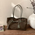 Détail d'un cabas en daim vert olive avec boucle décorative sur un banc en bois rustique - Vert