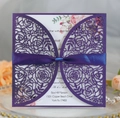 Close-up of laser-cut purple invitation with elegant rose patterns and a silk ribbon bow - Deep purple