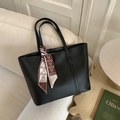 Detail of a black leather tote bag with a decorative floral silk scarf on a sofa - Black