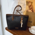Fashionable woven black tote bag with brown trim and beaded charm on wooden desk - Black