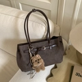 Detail of dark brown suede tote bag with metal buckle and plush bear pendant on sofa - Brown