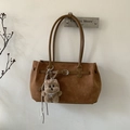 Detail of vintage brown suede tote bag with buckle strap and cute bear charm on wall - Caramel color