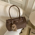 Detail of dark brown leather tote bag with plush bear charm on a cozy cream sofa - Brown
