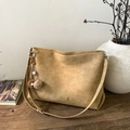 Macro shot of faux suede tote bag with cross stitching, logo tag, and stylish charm - Camel With Charms