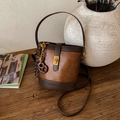 Bolso saco retro de cuero marrón con cierre dorado y bandolera en mesa de madera - Marrón con colgante