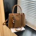Bolso cubo marrón de grano lichi con placa de logo y colgante de cuentas sobre libro - Marrón