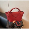 Detailaufnahme einer roten Eimer-Handtasche mit Litschimuster und goldener Hardware - Burgunderrot