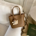 Gros plan sur le sac seau en cuir caramel avec texture grainée et charm en peluche doux - Brun Thé