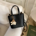 Detail of black lychee grain leather bucket bag with gold hardware and plush charm on sofa - Black