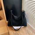 Minimalist black matte hobo bag with adjustable strap and visible stitching on wood bench - Black