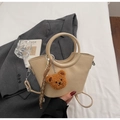 Close-up of beige leather bucket bag with circular handle and cute teddy bear charm - Off-white