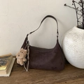 Detail der dunkelbraunen Wildleder-Hobo-Tasche mit Plüsch-Hundeanhänger auf Holztisch - Kaffee mit Anhänger
