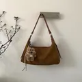 Braune Wildleder-Halbmondtasche an weißer Wand mit süßem Plüschbär-Anhänger-Detail - Braun mit Anhänger