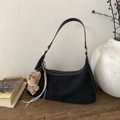 Detail der schwarzen Hobo-Tasche aus Wildleder mit Plüsch-Anhänger auf dem Holztisch - Schwarz mit Anhänger