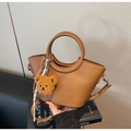 Detail of a brown leather bucket bag featuring a fixed round handle and plush bear charm - Tan