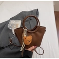 Deep brown bucket bag with circular handle and cute teddy bear charm on white linen - Coffee
