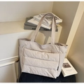 Detail einer großen cremefarbenen Stepptasche mit Seitentaschen auf einem Stuhl - Cremeweiß