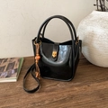 Detail of a glossy black bucket bag featuring a gold twist lock and a wooden bead tassel - PU Black (JC-1293)