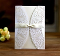 Detail of laser-cut lace invitation card featuring an ivory ribbon bow and floral pattern - Ivory