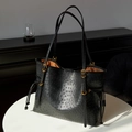 Detalle de bolso tote negro con textura de avestruz, aro dorado y forro marrón en mesa - Negro