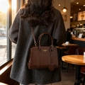 Borsa Boston retrò marrone scuro con logo dorato, indossata su un cappotto grigio al caffè - Marrone