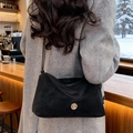 Sac fourre-tout noir en daim avec logo doré, porté par un mannequin dans un café chaleureux - Noir