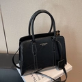 Glänzende schwarze Handtasche in Trapezform mit Griffen auf weißen Büchern - Schwarz