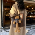 Dark brown leather tote bag with cute long-legged teddy bear pendant in winter setting - Coffee