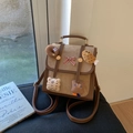 Detail van beige suède mini rugzak met pluche hangers en rode geruite strik detail - Khaki